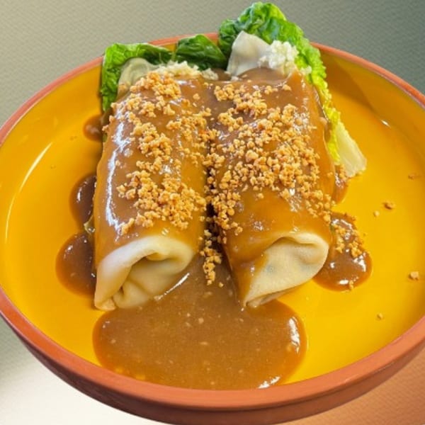 Two lumpia rolls covered in brown sauce and crushed peanuts, served with lettuce on a yellow plate.