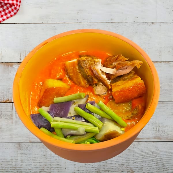 Kare-kare, a Filipino stew with meat, peanut sauce, eggplant, and green beans, in an orange bowl.