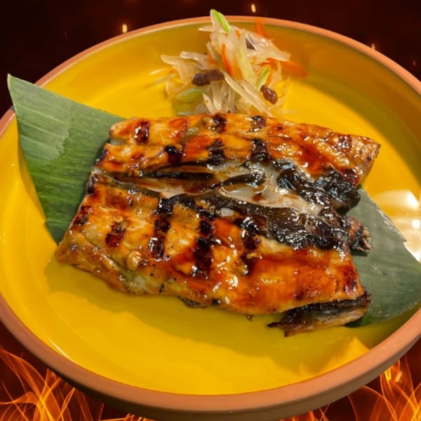 Grilled fish with a dark glaze, served on a banana leaf with a side of pickled vegetables.