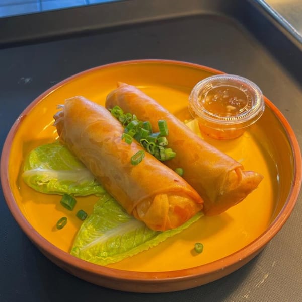 Two golden-brown Lumpia egg rolls on lettuce with chopped green onions and a side of dipping sauce.